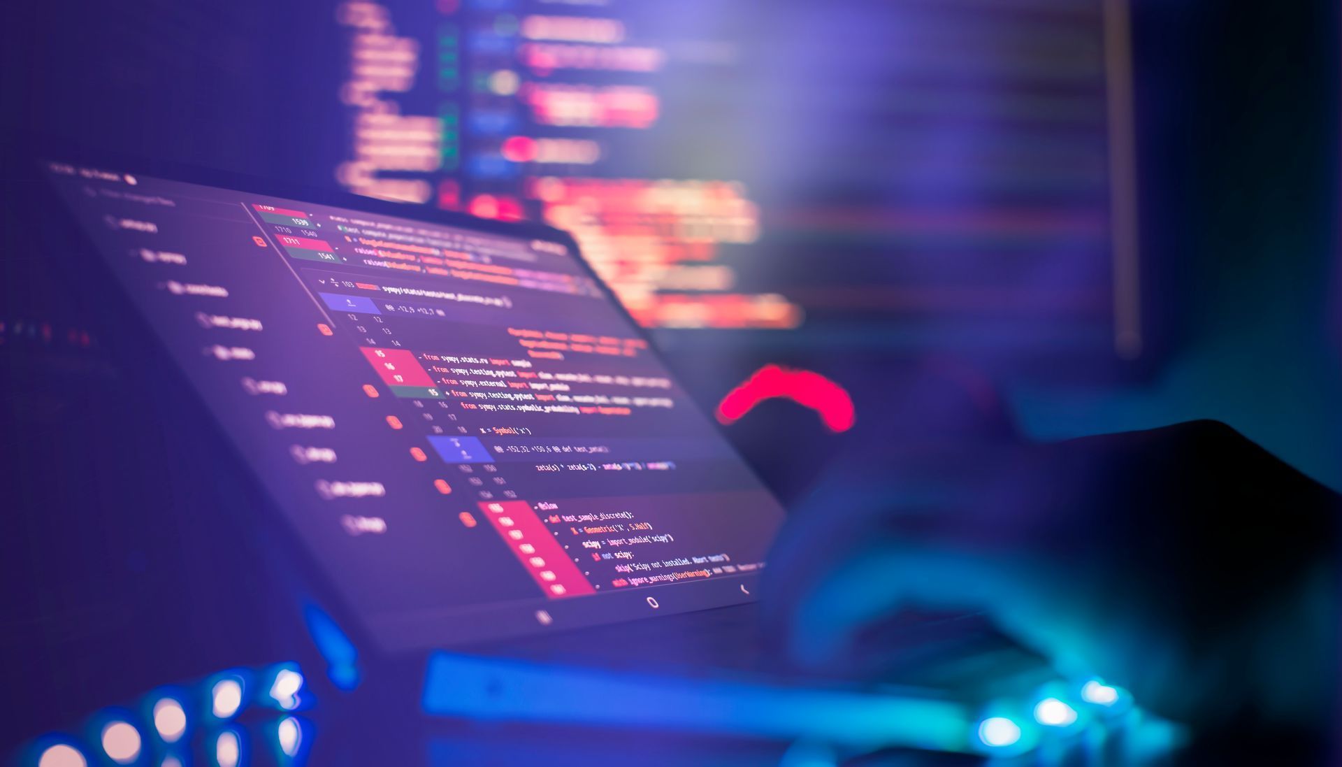 Person typing code on a laptop in a neon-lit workspace with blurred code on screen