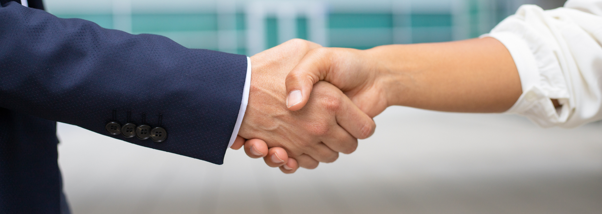 Business hands shaking in a close-up handshake, with a dark blue suit sleeve and a white shirt sleeve.