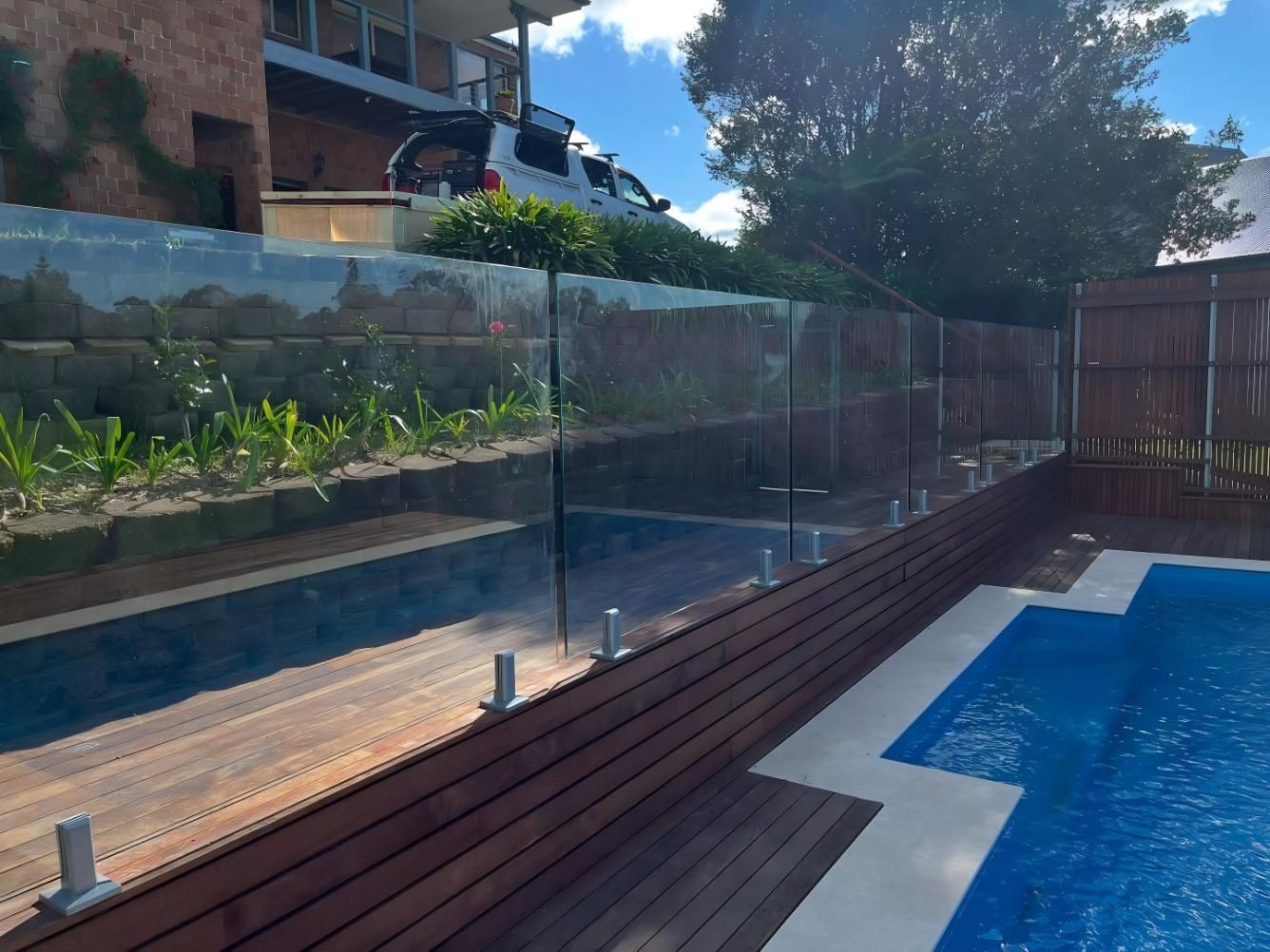 Glass Pool Fence on a Wooden Deck, With a Swimming Pool and Lush Greenery