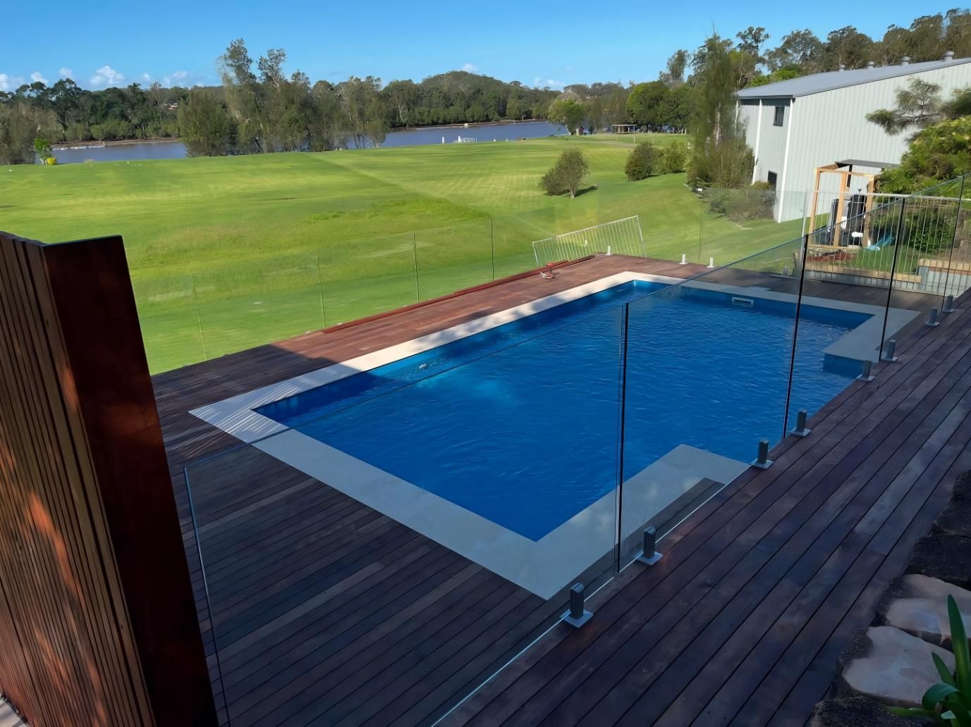 Pool Surrounded by Wooden Deck, Overlooking a Green Lawn, Trees, and a Building on a Sunny Day — Solitary Island Pools in Coffs Harbour, NSW