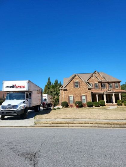 Moving trucks parked in front of a brick house on a sunny day.