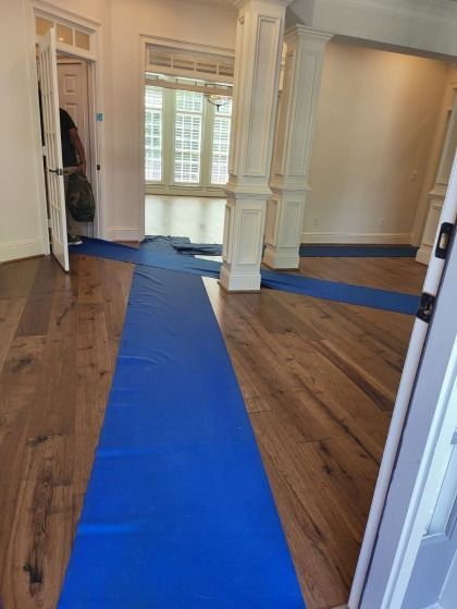 Blue floor protection runners on wood flooring in a house with white trim.