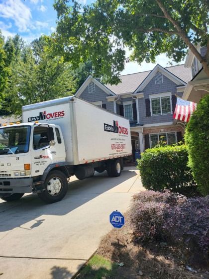 Moving truck parked in front of a gray house with a small American flag.