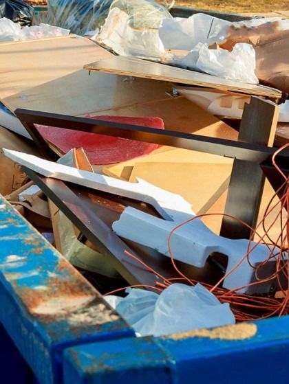 Pile of discarded construction debris in a blue dumpster; wood, foam, and wires visible.