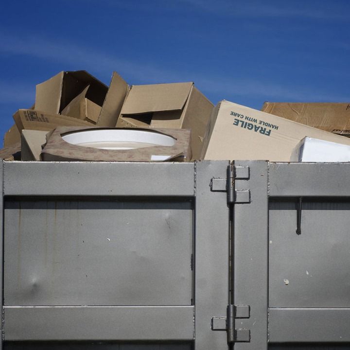 Cardboard boxes overflowing a metal bin against a blue sky.