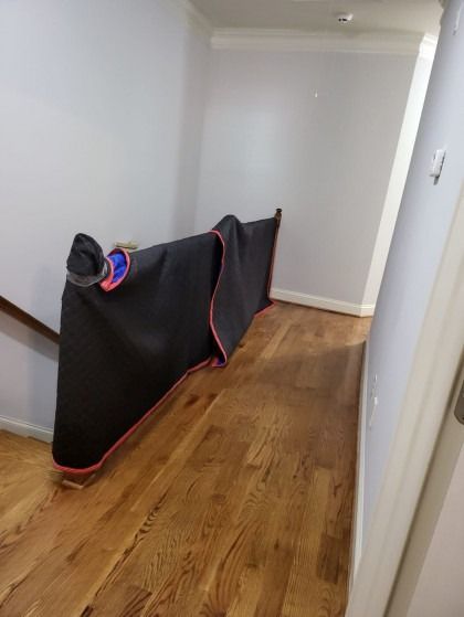 Wooden floored hallway with a black moving blanket leaning against a wall and staircase.