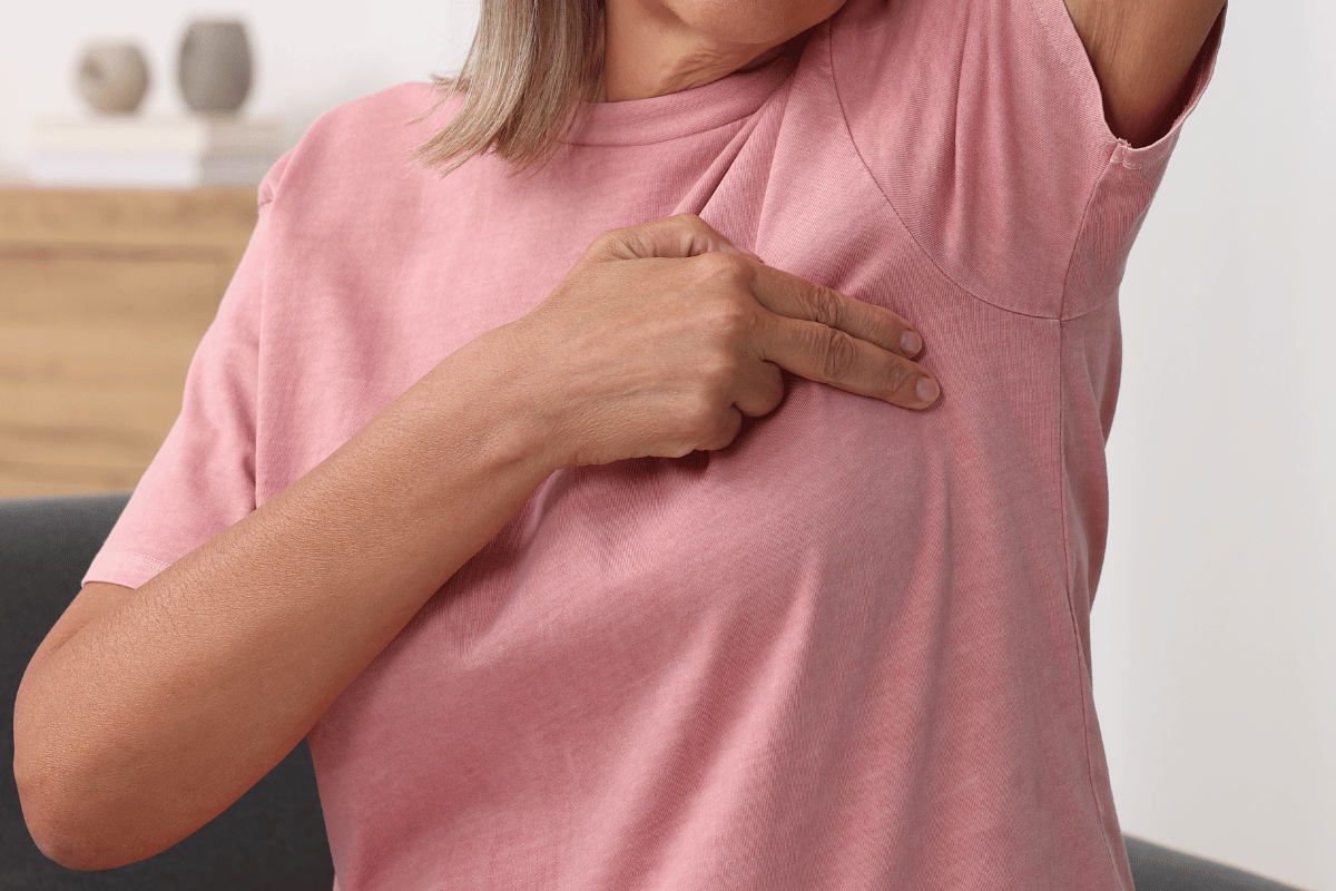 Woman in pink shirt pointing to her armpit.