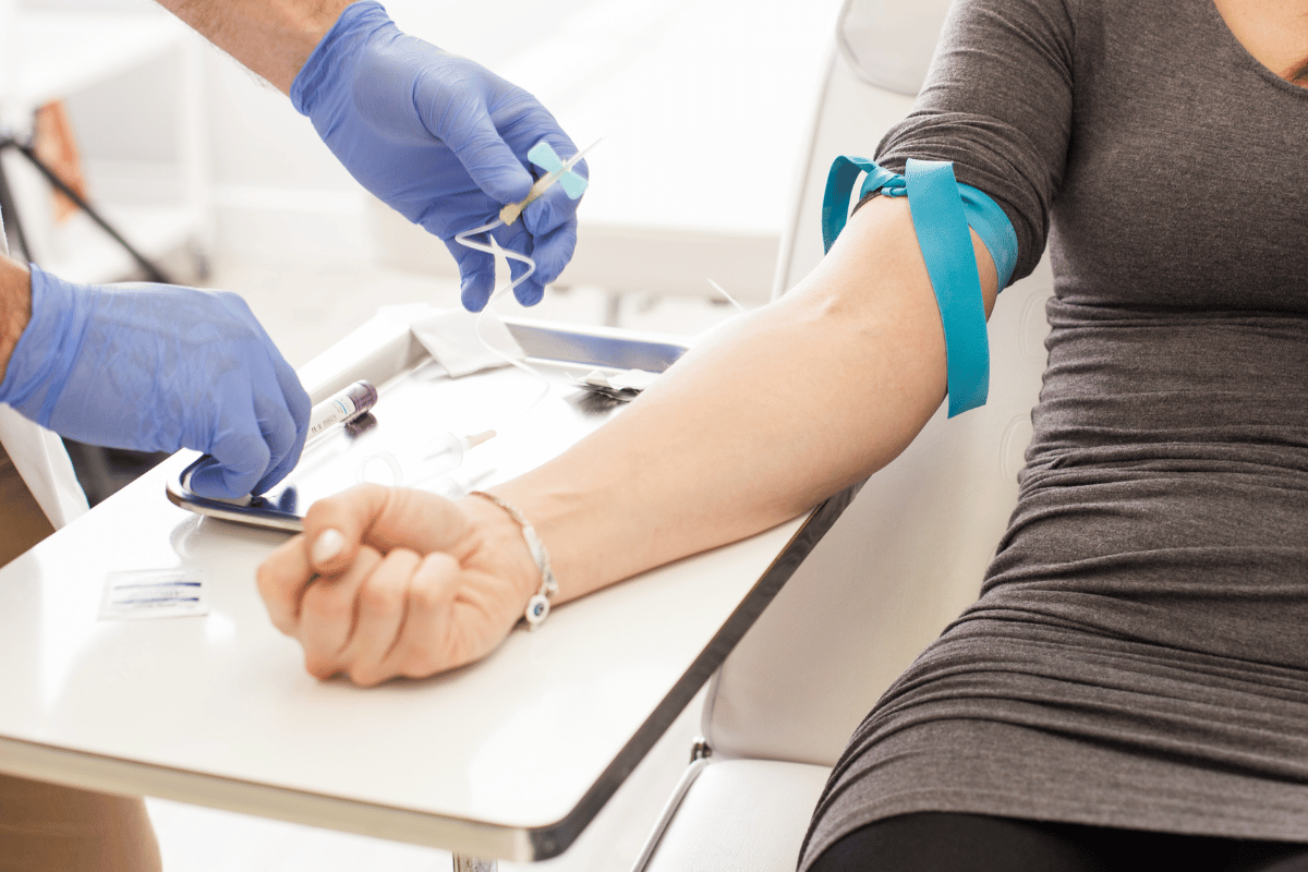 Person getting blood drawn; medical professional in blue gloves prepares needle on arm with tourniquet.