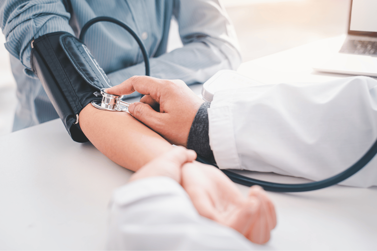 Doctor taking a patient's blood pressure in a medical office; stethoscope, arm cuff, white coat.