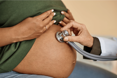 Pregnant woman's belly being examined with a stethoscope by a doctor.