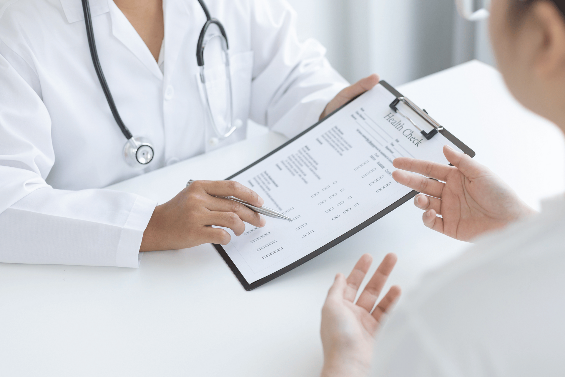 Doctor reviewing medical chart with a patient, white coats, stethoscope, office setting.