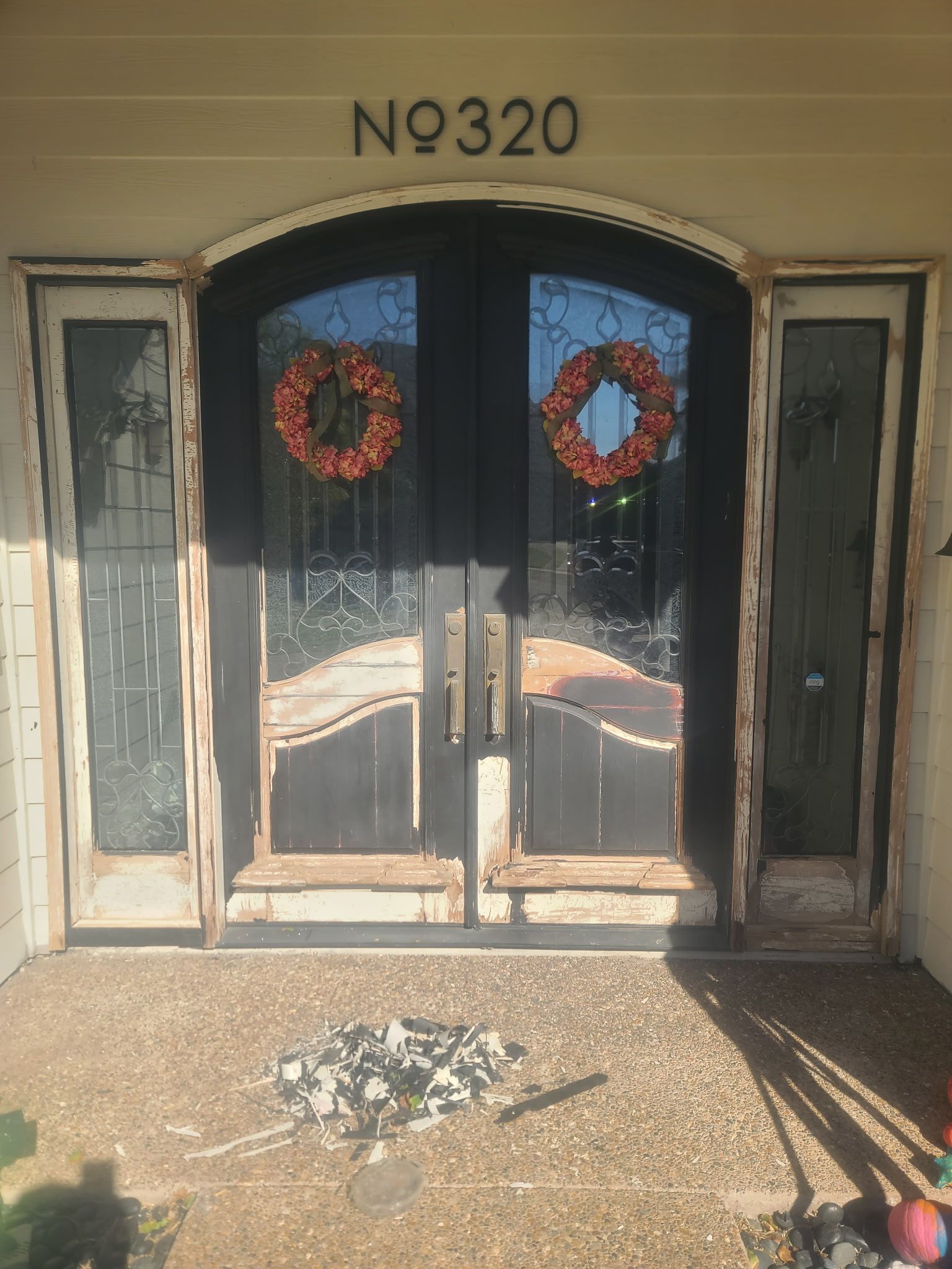 A double front door with black frames, glass panels, and wreaths, showing significant wood rot on the surrounding trim.