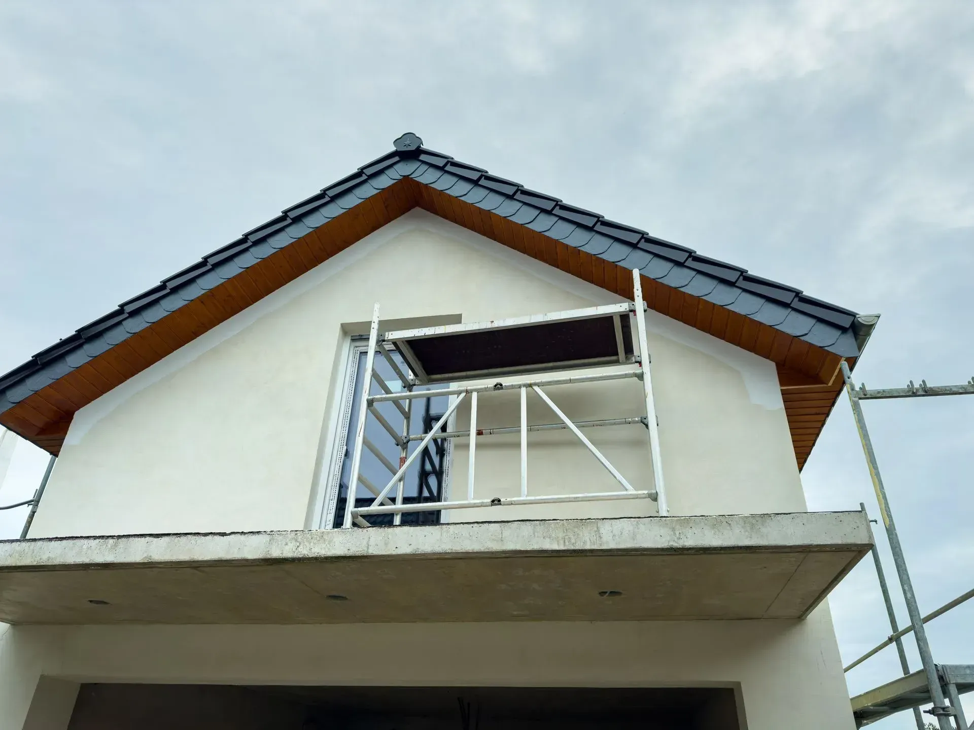 A light-colored house facade under construction with scaffolding positioned in front of an upper-story window.