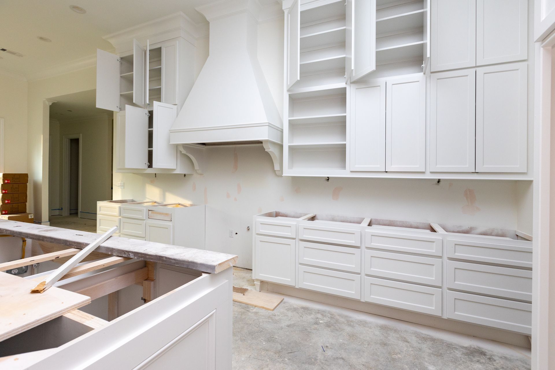 An unfinished kitchen featuring white cabinetry, a matching range hood, and base cabinets with drawers under construction.