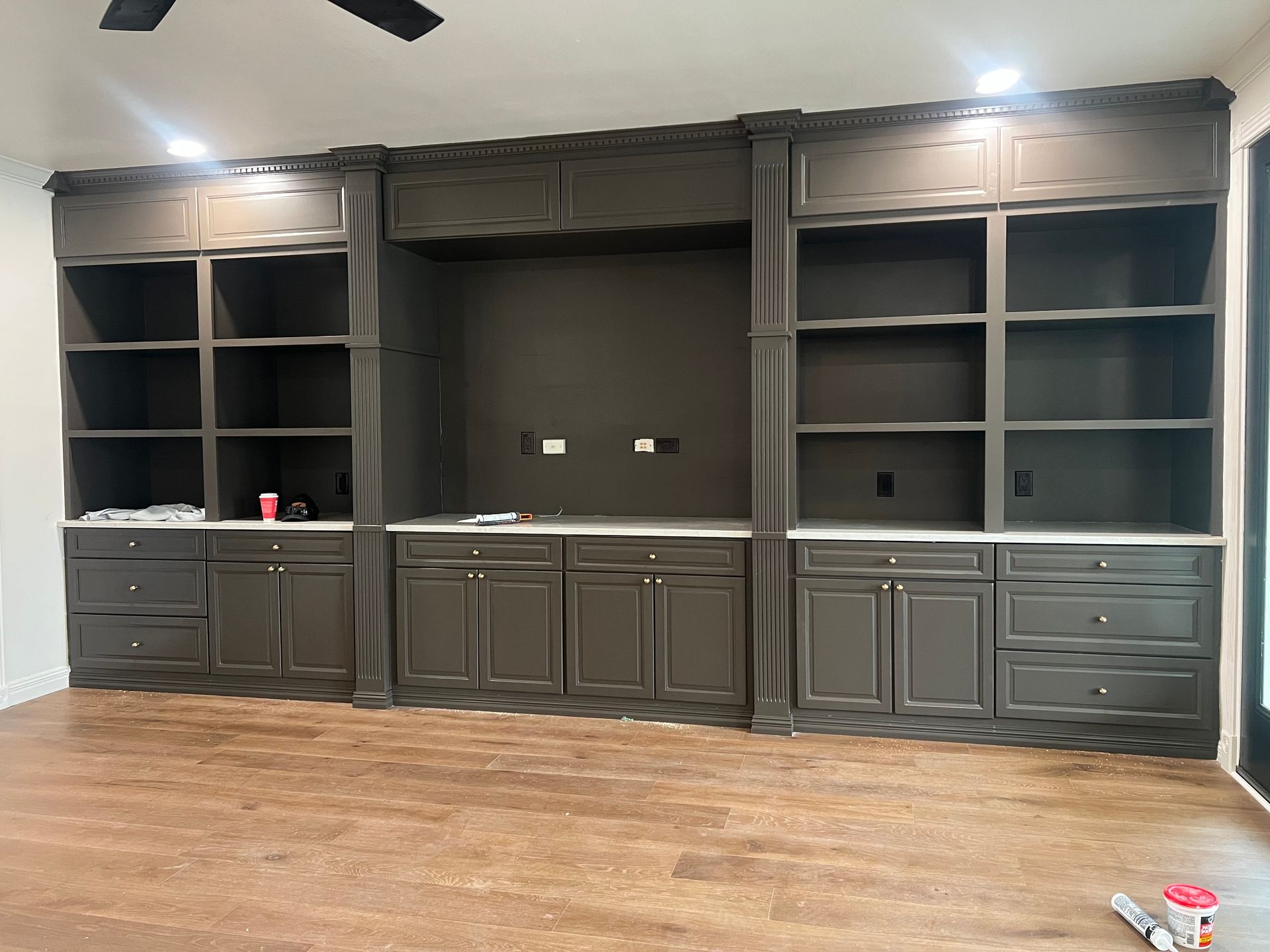 A large, dark brown custom built-in entertainment center with open shelving, cabinets, and drawers against a white wall.