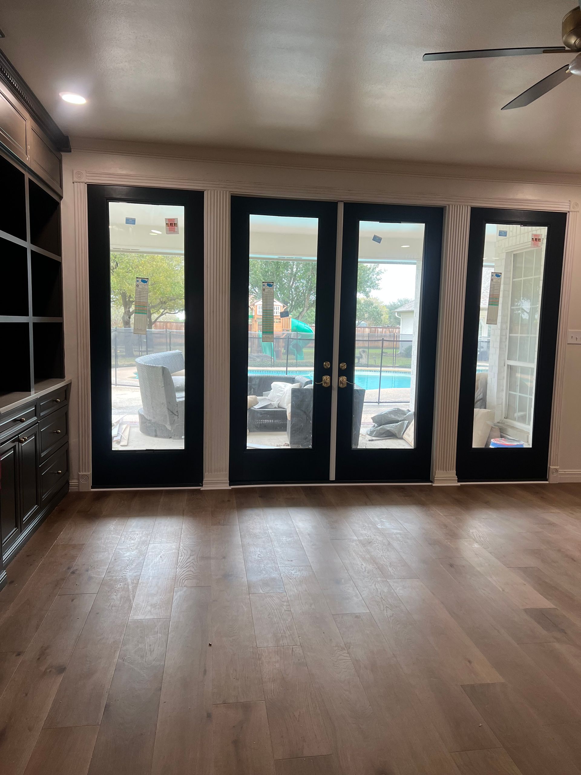 A room with wood floors and four black-framed glass doors looking out to a backyard pool area.