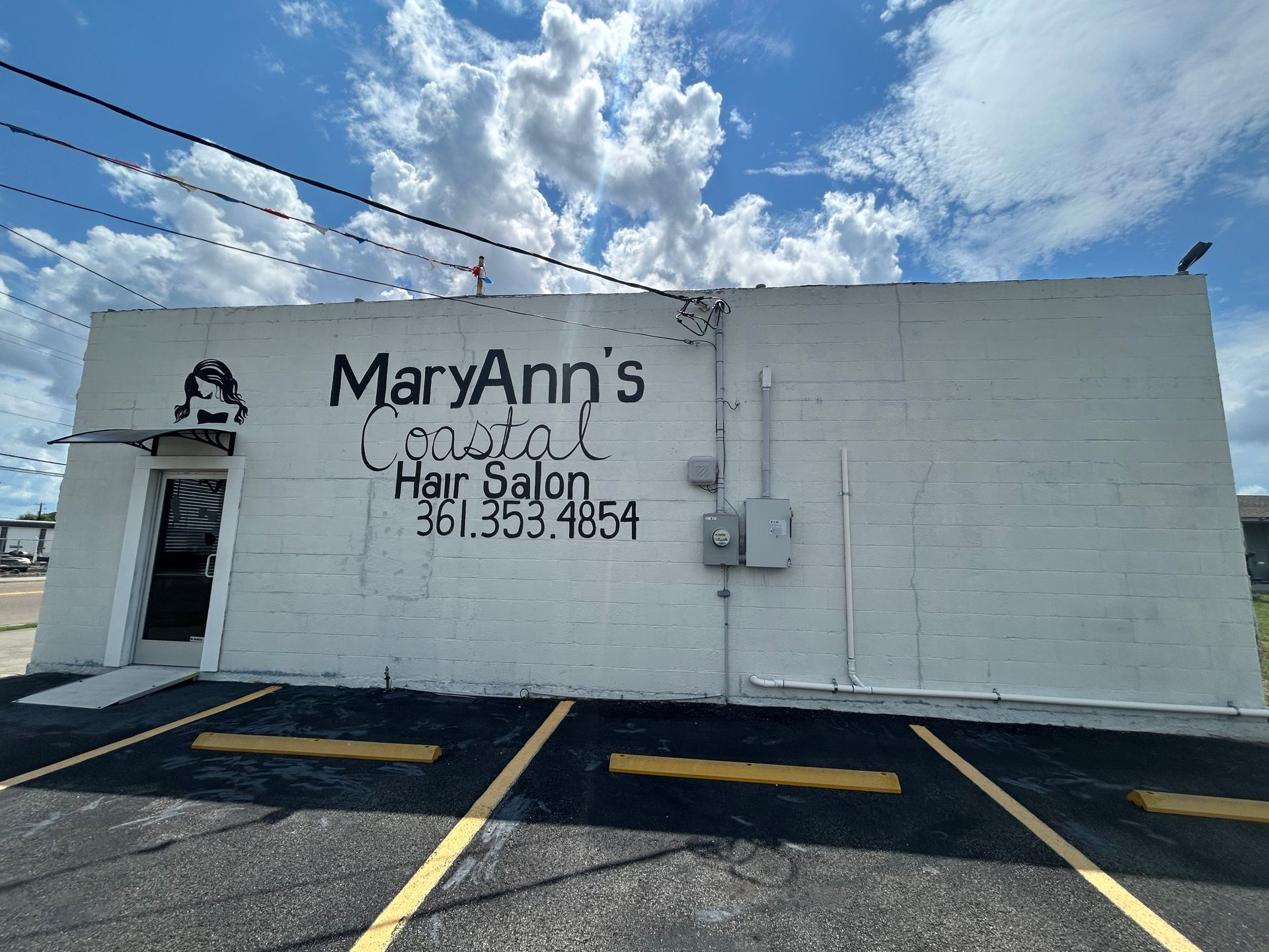 A white cinder block building for MaryAnn’s Coastal Hair Salon with its phone number, 361-353-4954, painted on the exterior.