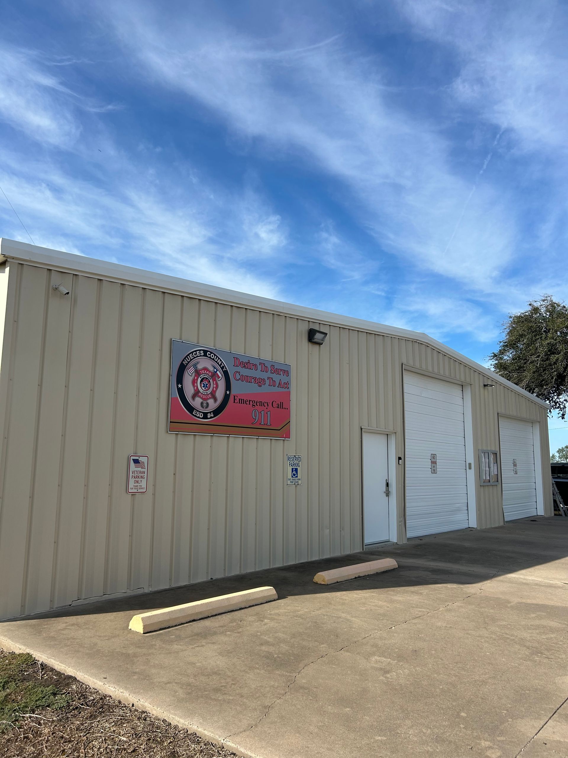 A tan industrial building featuring a fire department logo on the side with two large white garage doors under blue sky.