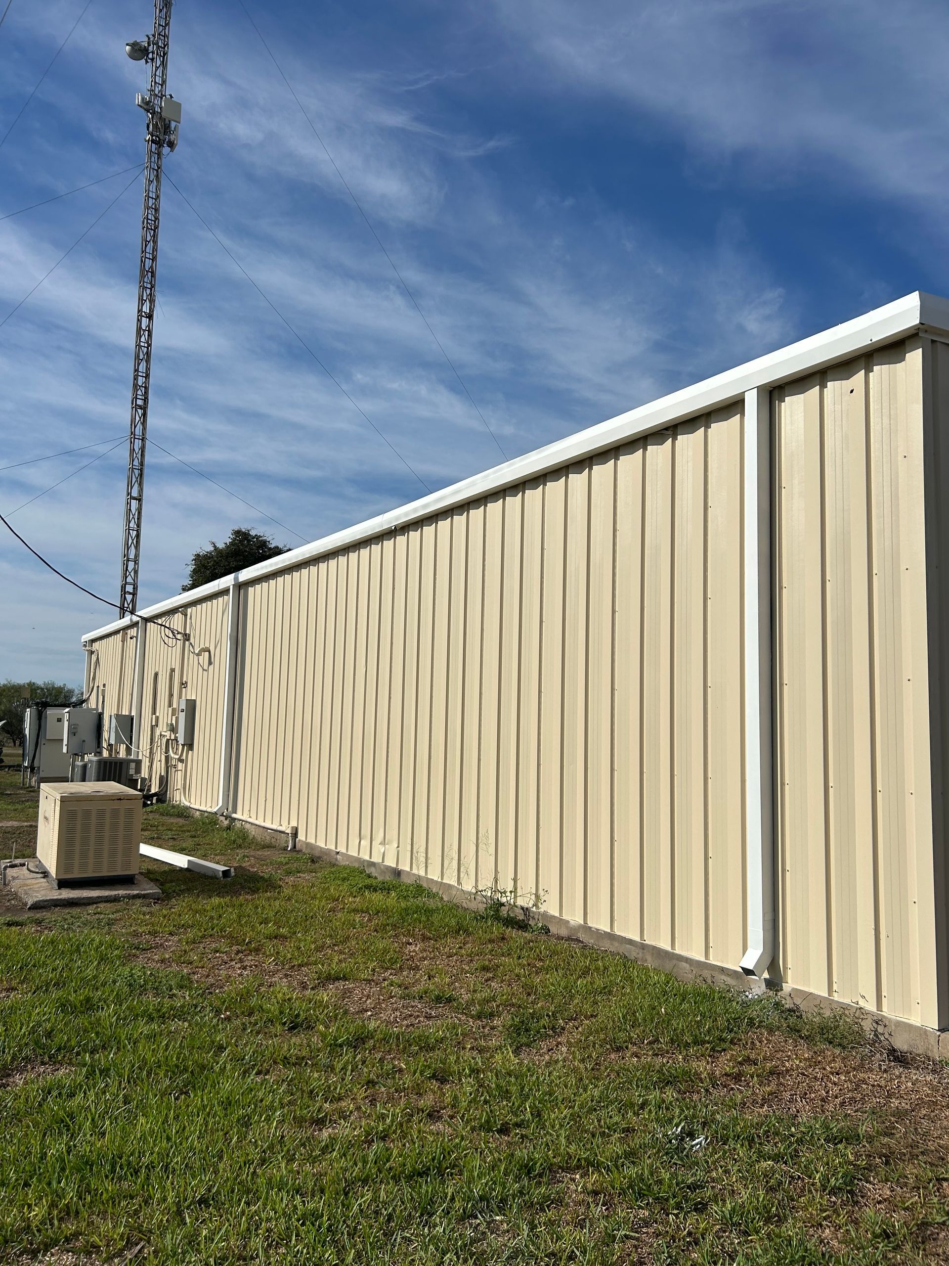 Tan metal storage building with a tall communications tower against a blue sky.