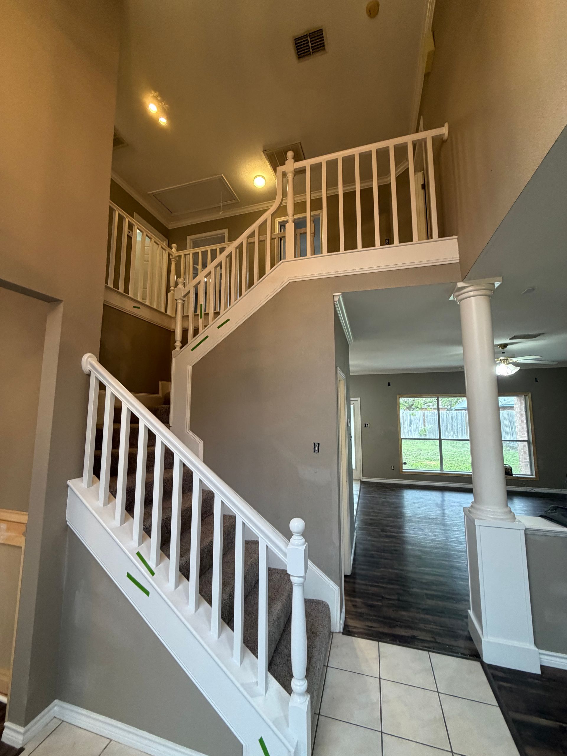 A grand staircase with white railings, grey carpeted steps, and beige walls in a high-ceilinged home entrance.