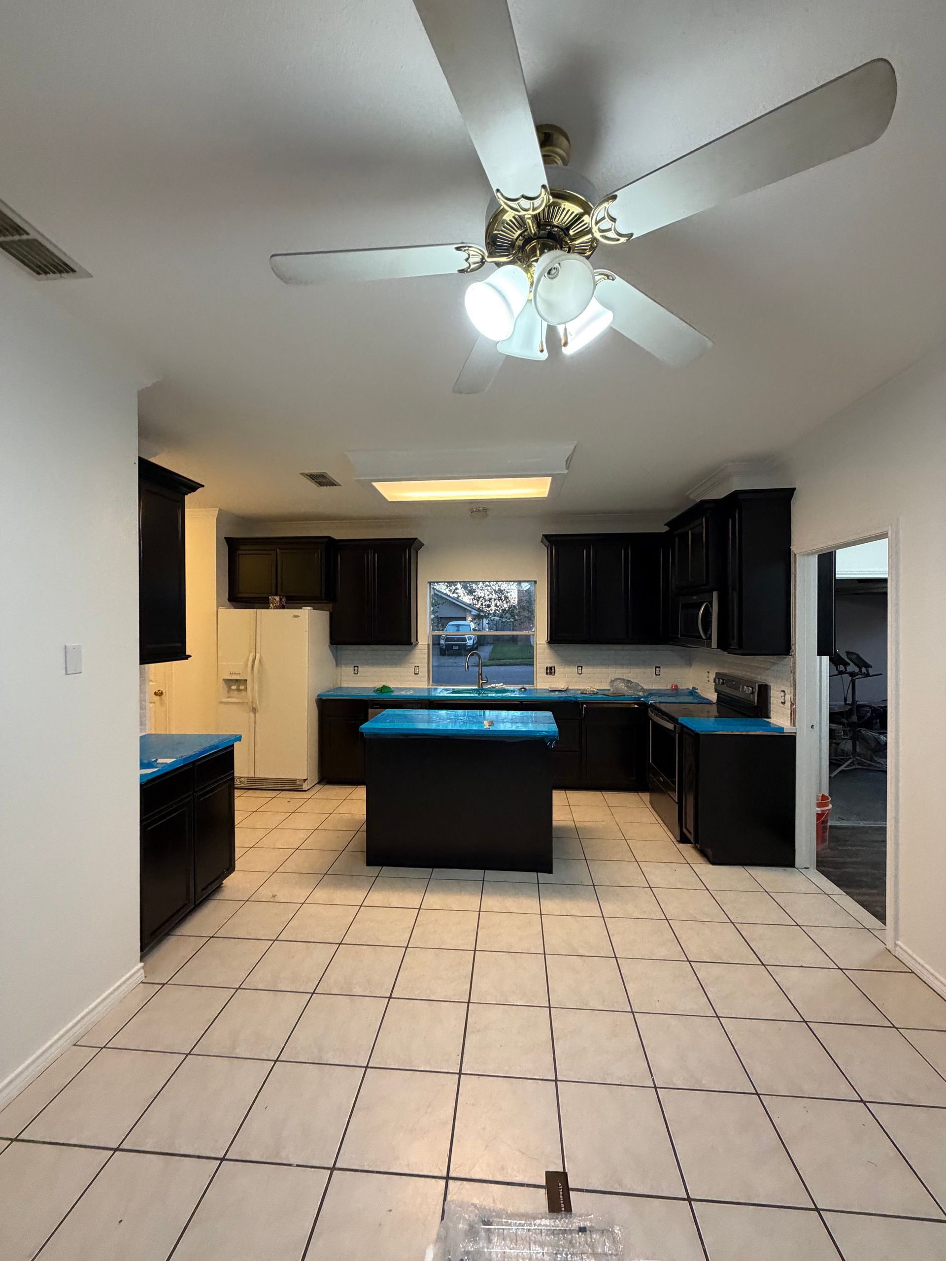 A kitchen renovation featuring black cabinets, blue protective film on countertops, and a ceiling fan over light tile.