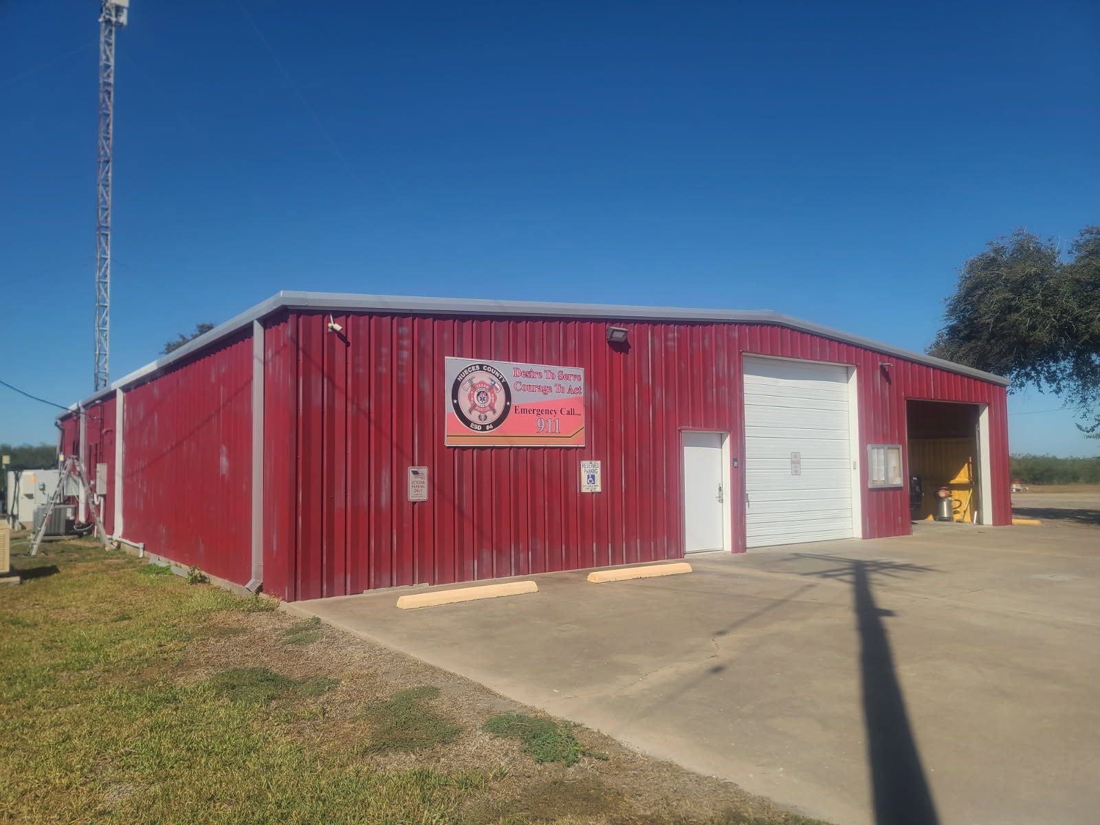 A red metal warehouse building under a clear blue sky, featuring a white door and a rollup garage door with a sign above.