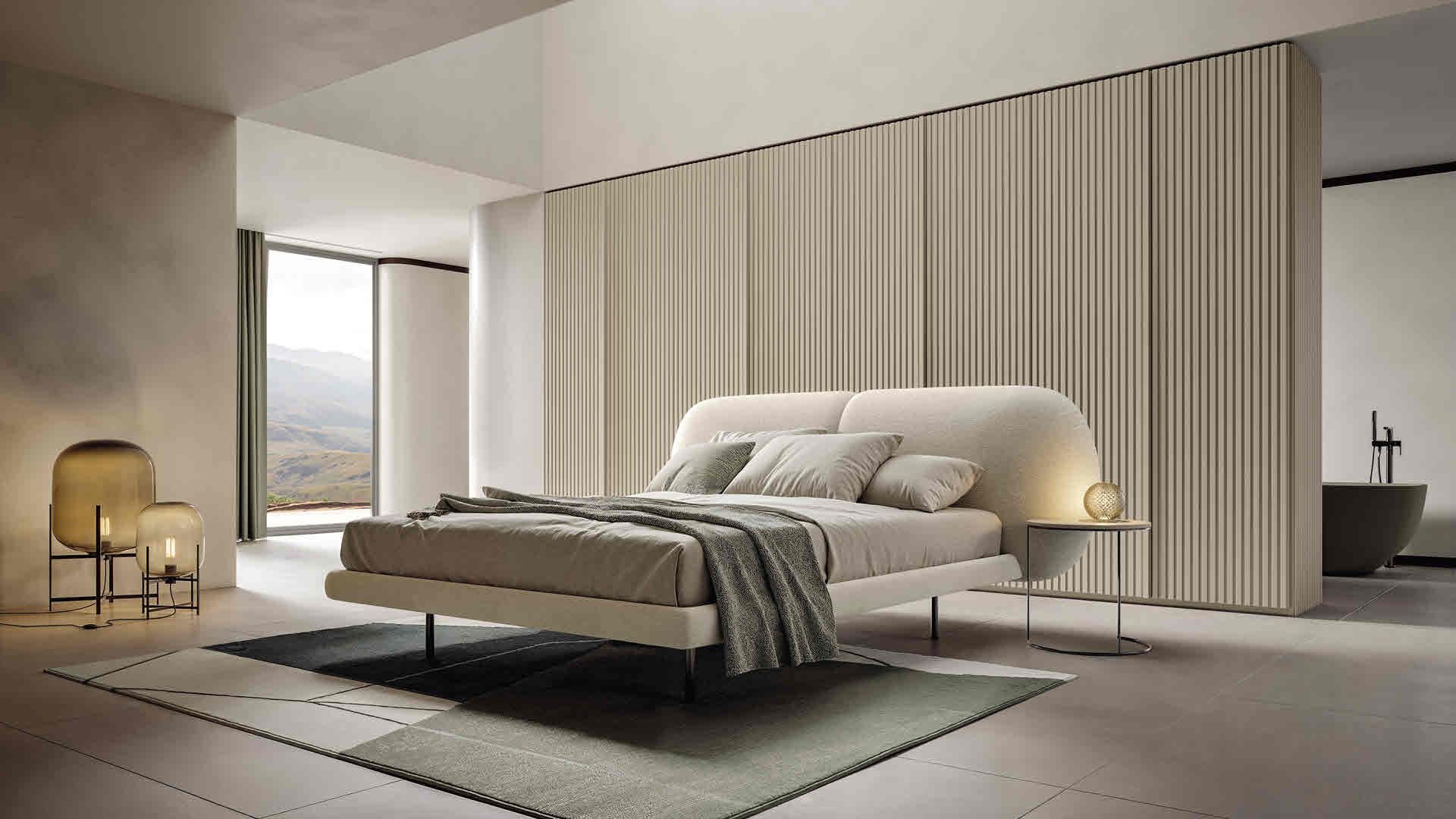 Camera da letto minimalista con letto basso, tonalità neutre e pannelli in legno dal pavimento al soffitto.