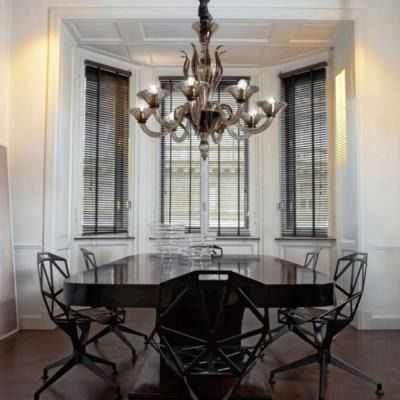 Elegante sala da pranzo con sedie scure, tavolo ovale, lampadario e alte finestre con persiane.
