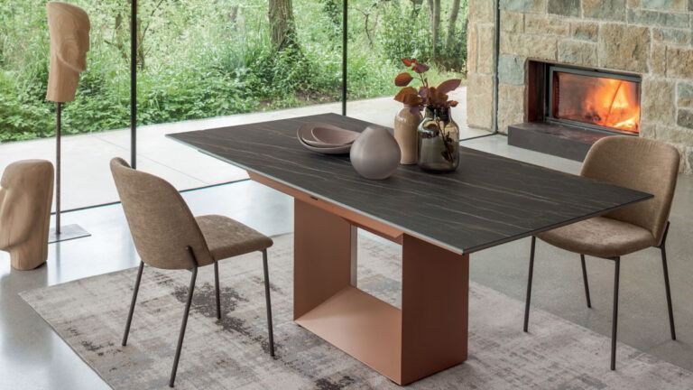 Sala da pranzo moderna con tavolo in legno, quattro sedie, tappeto e camino accanto a un'ampia parete vetrata con vista sul verde.