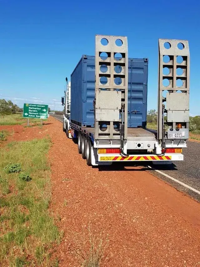 A Semi Truck with A Blue Container on The Back Is Driving Down a Dirt Road — Smillie Transport Pty Ltd in Two Mile, QLD