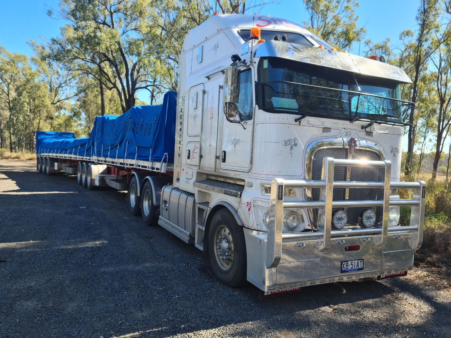 A Semi Truck Is Driving Down a Road Next to A Row of Shipping Containers — Smillie Transport Pty Ltd in Two Mile, QLD