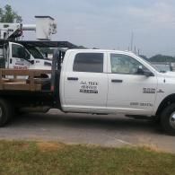 A white commercial utility truck with a boom lift parked on a grassy verge under an overcast sky.