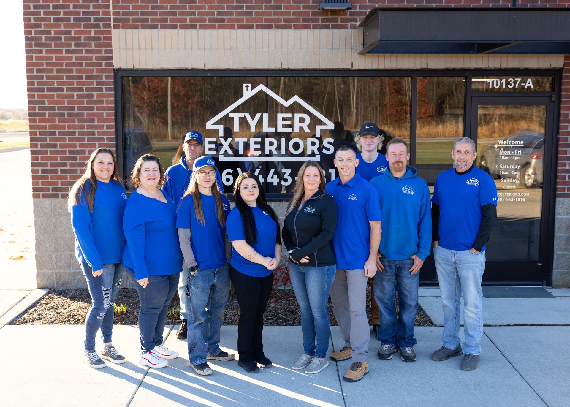 Tyler Exteriors staff posing in front of their business, wearing blue shirts. Brick building.