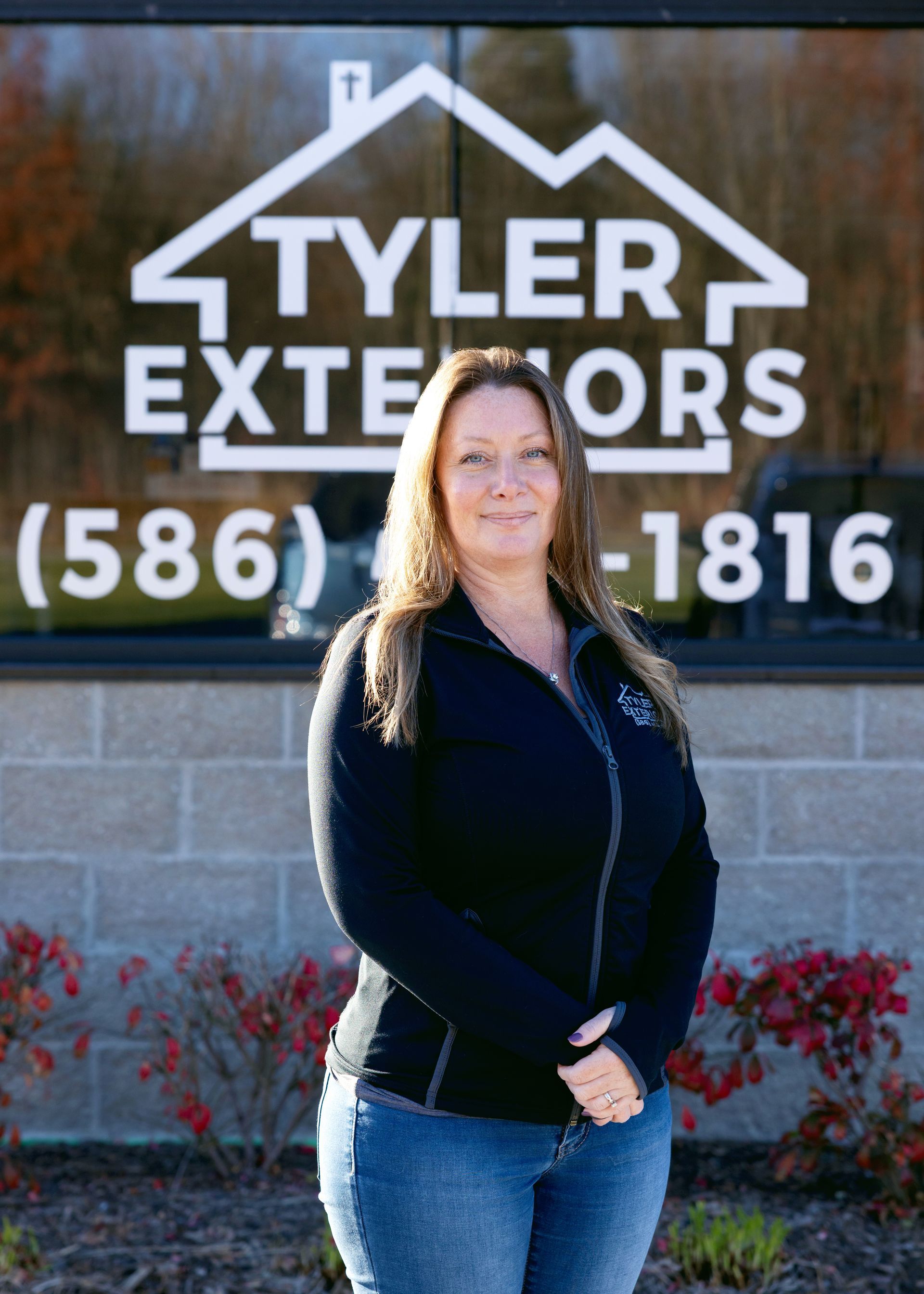 Woman in front of Tyler Exteriors sign, wearing blue jeans and a black jacket.
