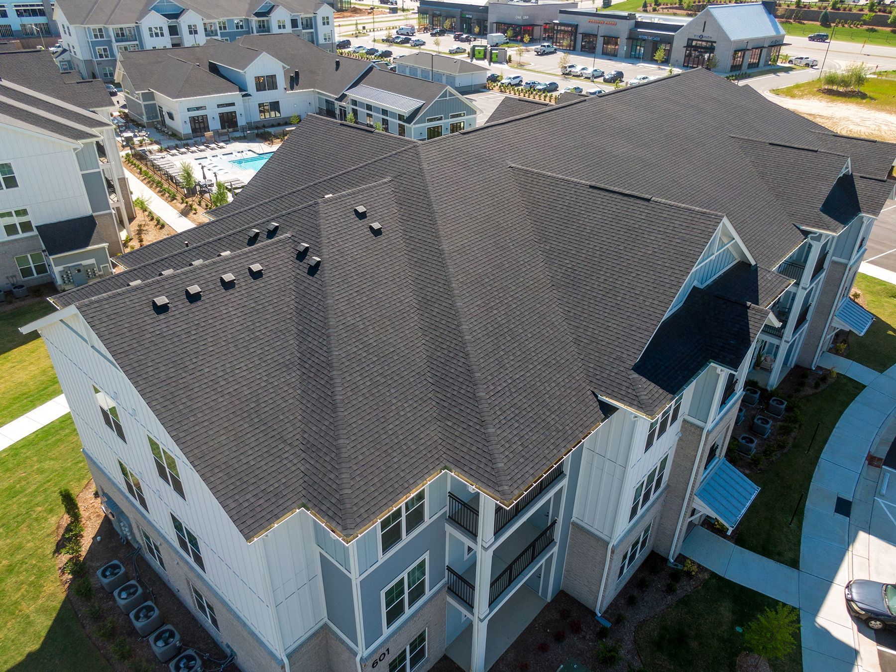 Aerial view of a multi-story apartment building with dark gray shingle roof and light blue siding.