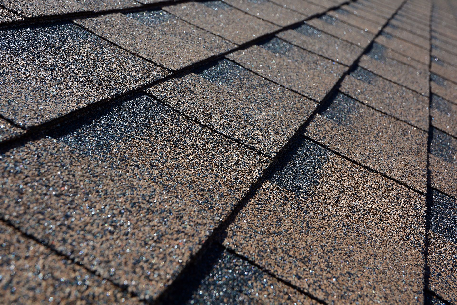 Close-up of brown asphalt roof shingles on a sunny day.
