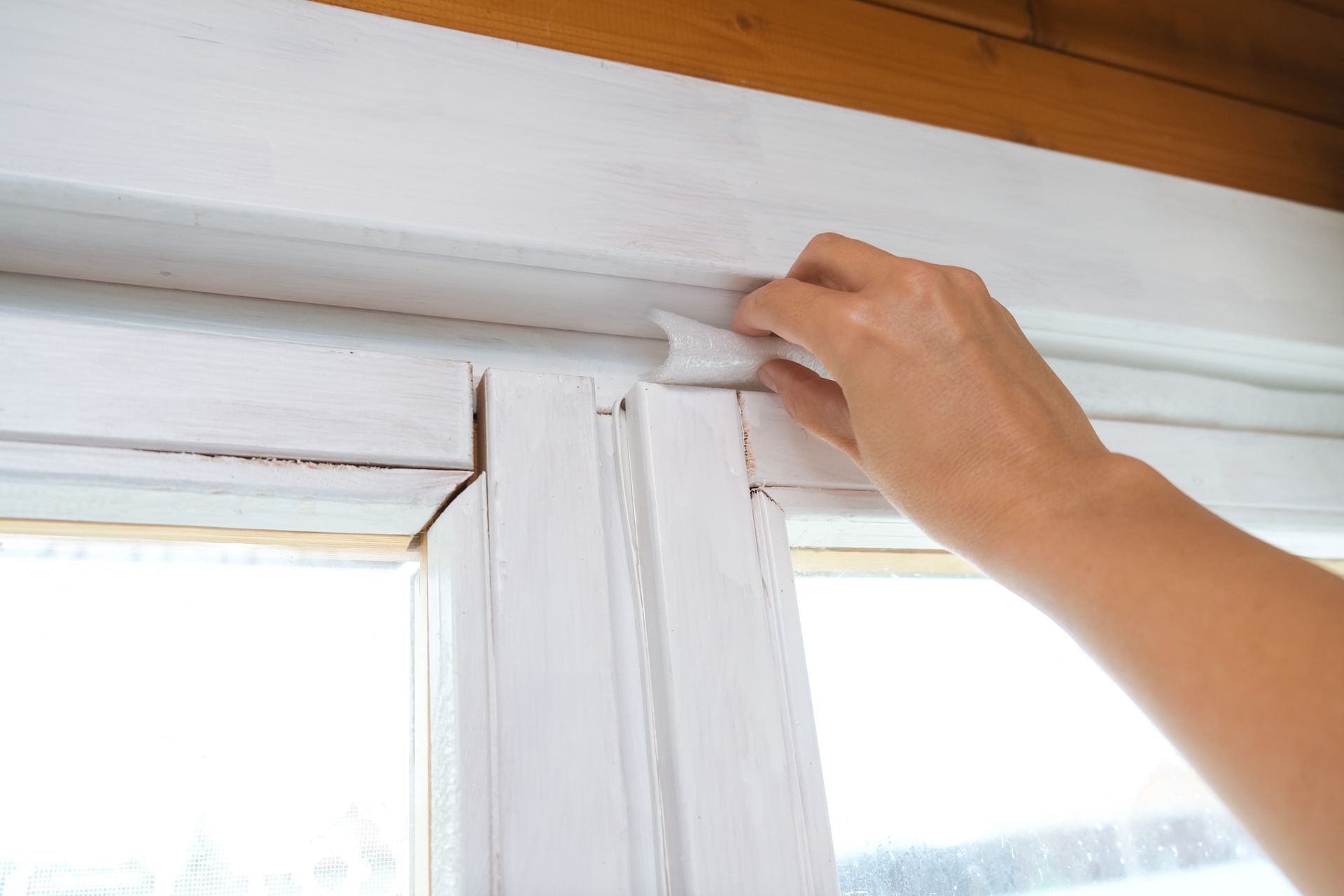 Person peeling white weather stripping from a painted window frame.