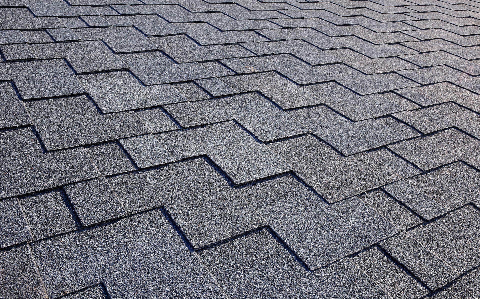 Dark gray asphalt shingles on a rooftop, arranged in a zig-zag pattern.