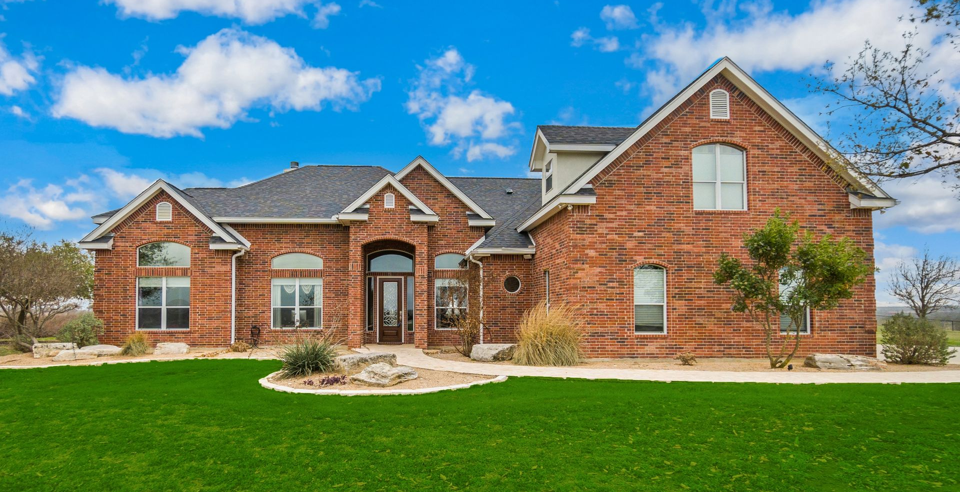 Red brick house with green lawn against a blue sky with fluffy clouds.