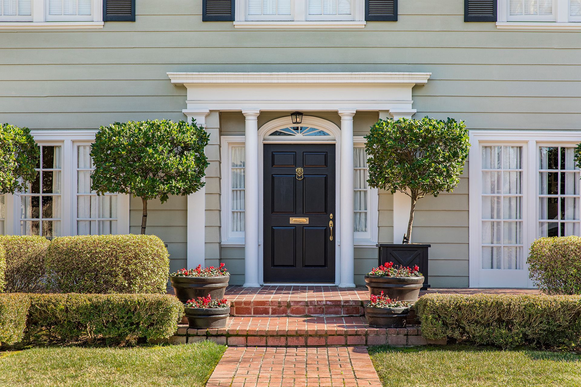 Black front door with white trim, flanked by symmetrical bushes and trees.