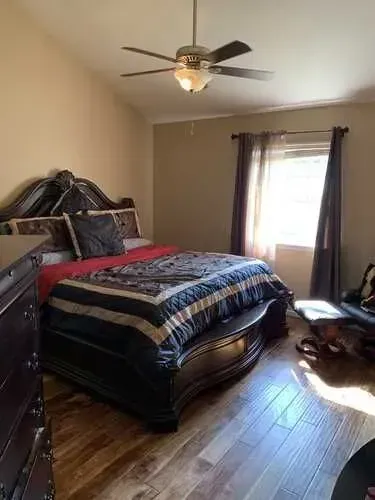 A bedroom with a bed , dresser , and ceiling fan.