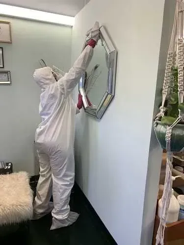 A person in a protective suit is hanging a mirror on a wall.