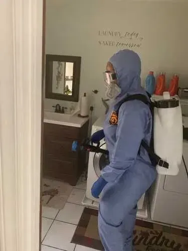 A person in a protective suit is spraying a room with a sprayer.