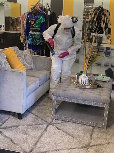 A man in a protective suit is disinfecting a living room.