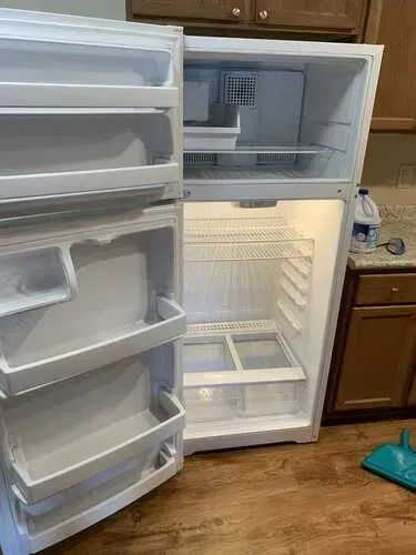 An empty refrigerator is sitting in a kitchen with the door open.
