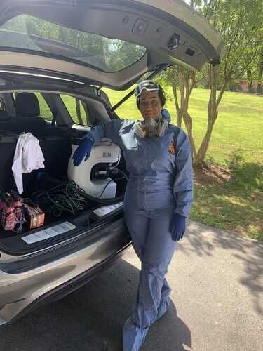 A woman in a protective suit is standing next to the back of a car.