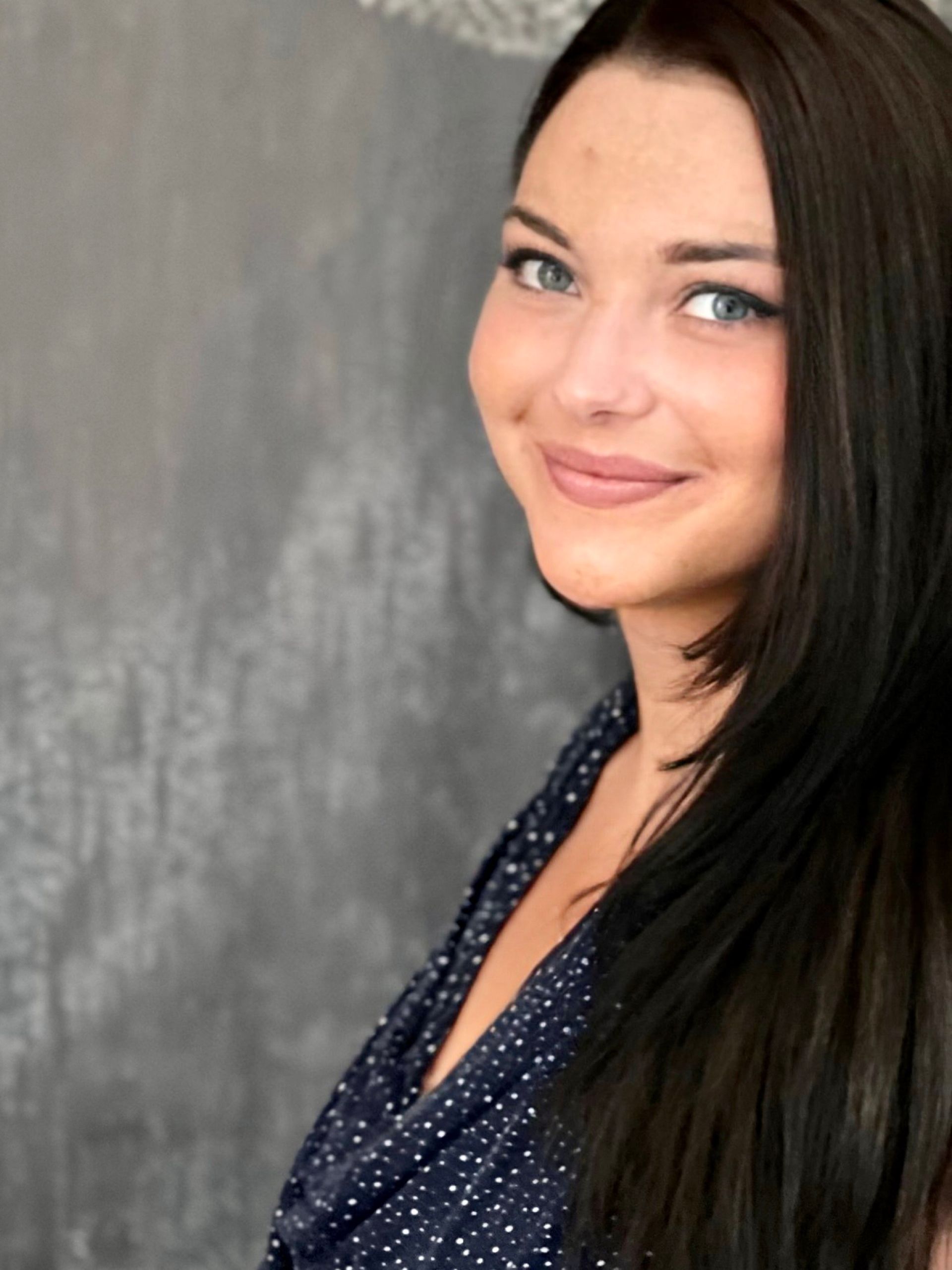 Eine Frau mit langen dunklen Haaren und blauen Augen lächelt in die Kamera