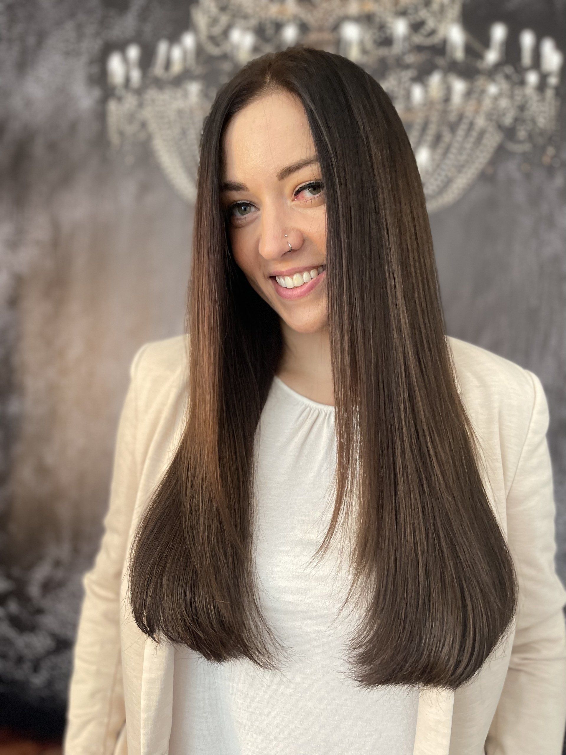 Eine Frau mit langen braunen Haaren lächelt vor einem Kronleuchter.