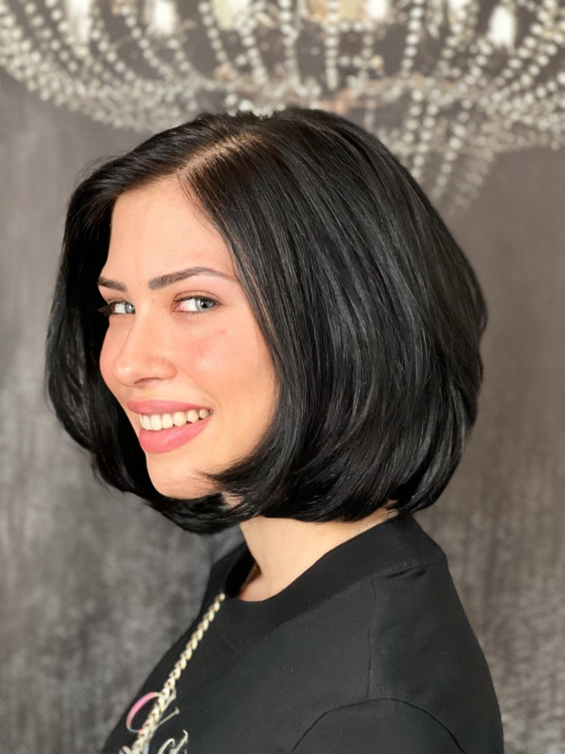 Eine Frau mit kurzen schwarzen Haaren lächelt vor einem Kronleuchter.