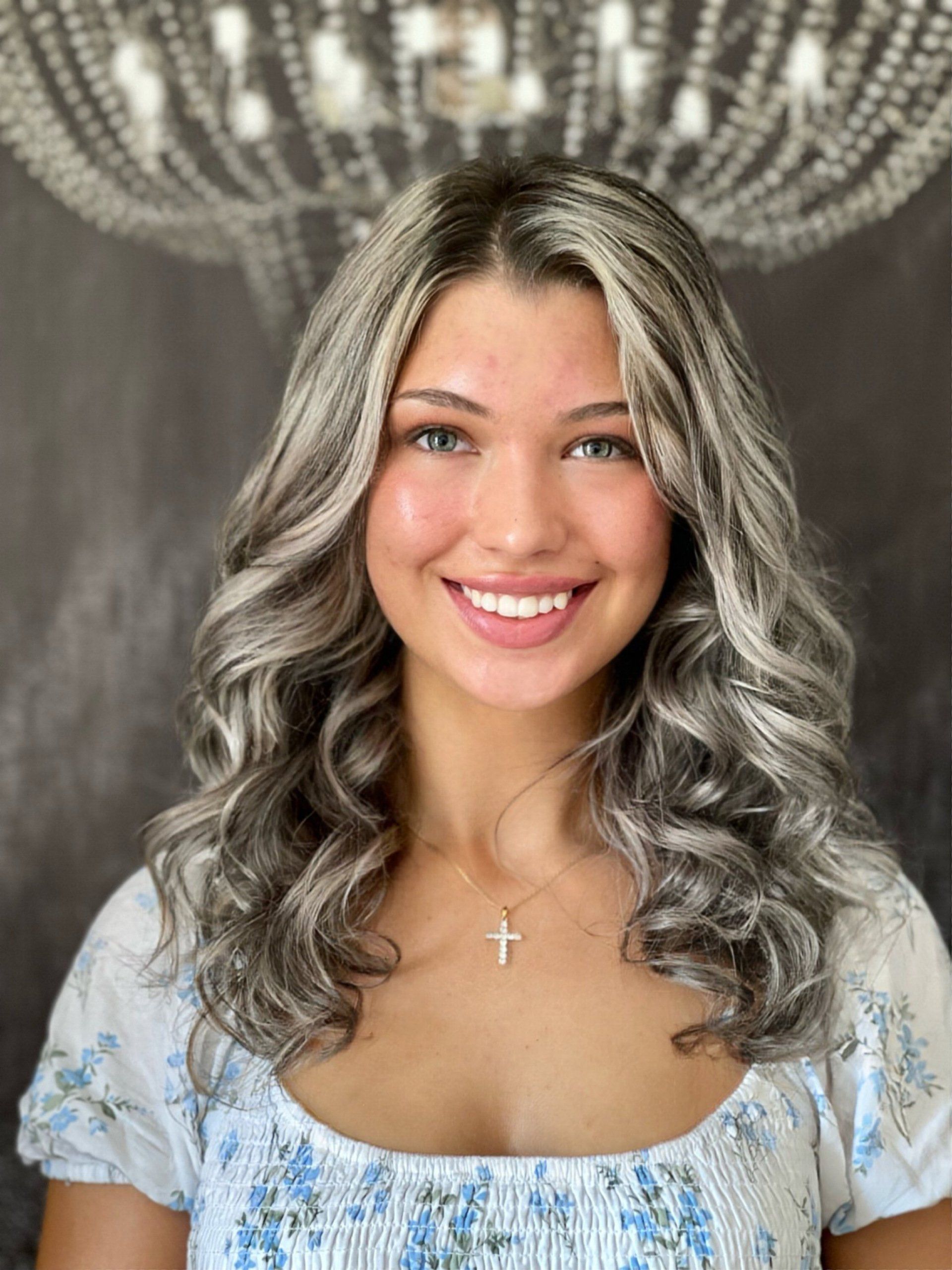 Eine Frau mit grauem Haar lächelt vor einem Kronleuchter.